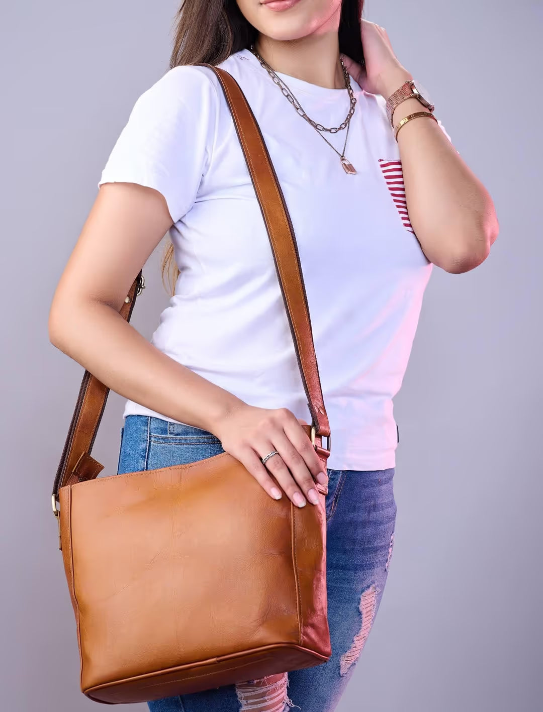 Person holding a brown leather handbag against a plain background