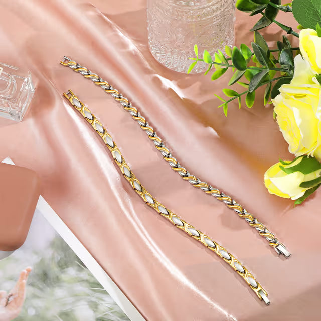 Gold and silver bracelet on a pink fabric background with flowers and a glass container.