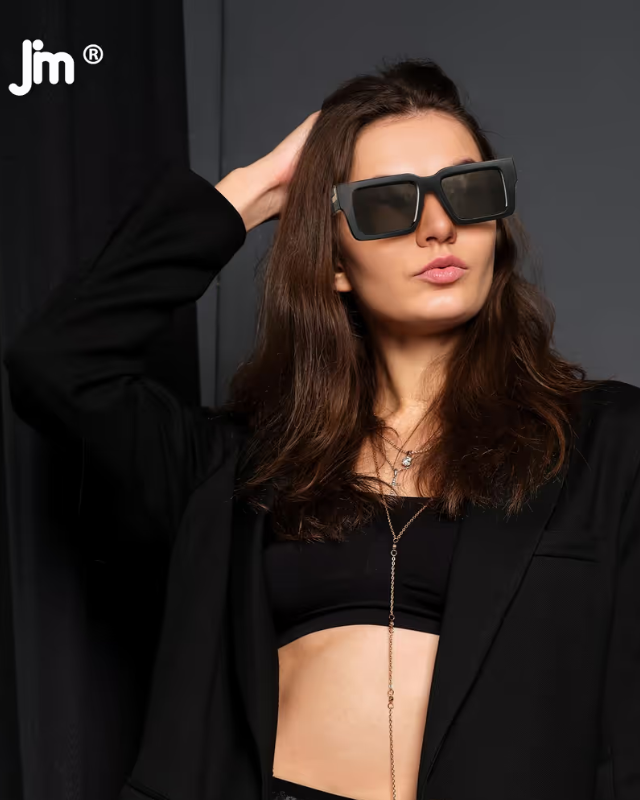 Woman wearing large sunglasses with a blurred background and 'jm' logo.