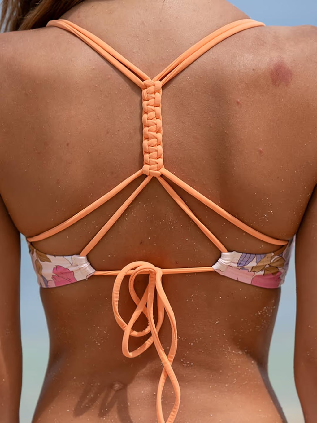 Person wearing a bikini with an intricate peach-colored strap design on a blurred natural background