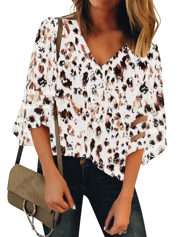 Woman wearing a floral blouse with cut-out details, holding a beige handbag.