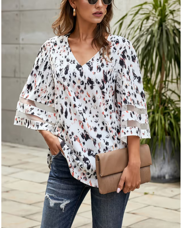 Woman wearing a floral blouse with sheer sleeves and holding a beige clutch.