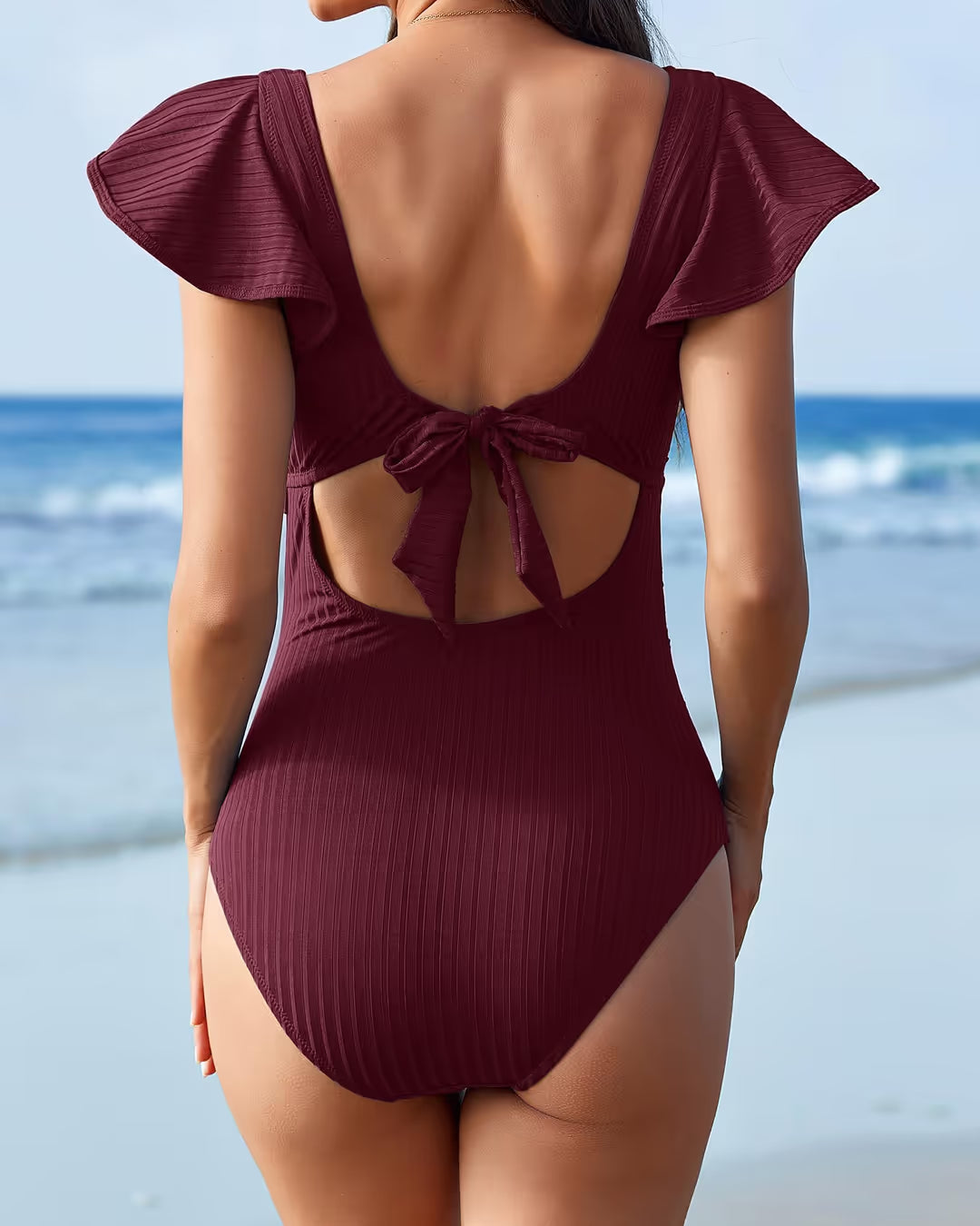 Woman wearing a burgundy swimsuit with ruffled sleeves on a beach.