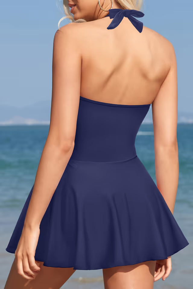 Woman wearing a blue dress with a bow at the back, standing on a beach.